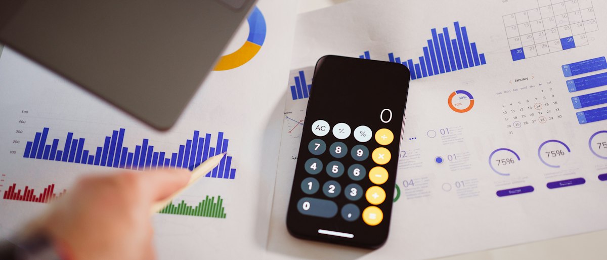 Calcolatrice sullo schermo di uno smartphone appoggiato su report con grafici finanziari